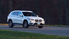 a white bmw suv driving down a road next to some grass and trees in the background