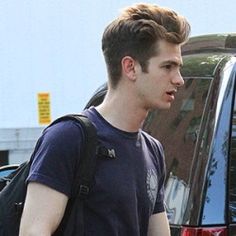 a young man with a backpack is walking towards a parked car and talking to someone