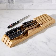 four knives in a wooden holder on a white marble counter top next to a knife sharpener