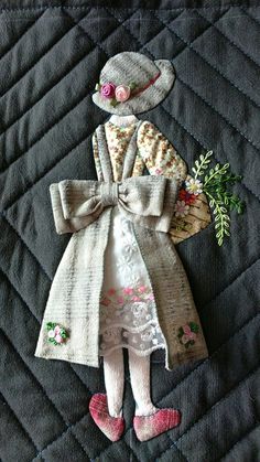 an embroidered doll is sitting on top of a quilt