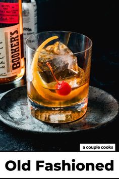 a glass filled with ice and a cherry sitting on top of a plate next to bottles