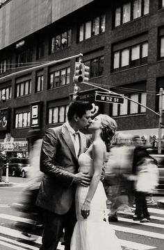 a bride and groom kissing on the street in front of a traffic light with blurry pedestrians