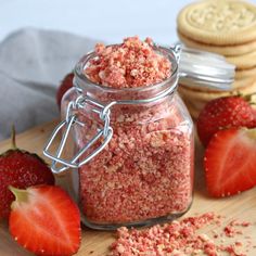 a jar filled with pink sugar next to strawberries and cookies on a cutting board