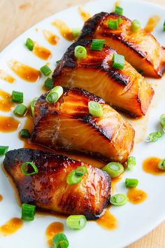 three pieces of fish on a plate with sauce and green onions