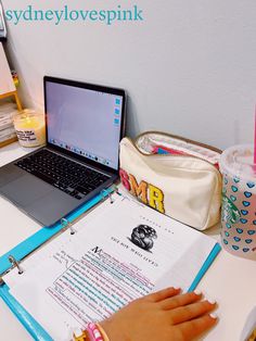 a person's hand on a notebook next to a laptop computer and other office supplies