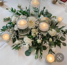 white flowers and candles are arranged on the table for a centerpiece with greenery