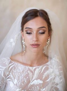 a woman wearing a wedding veil with flowers and pearls on the head is looking down at her face