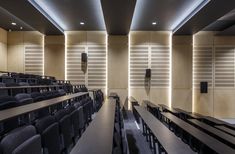 an empty lecture hall with rows of black chairs and lights on the wall behind them