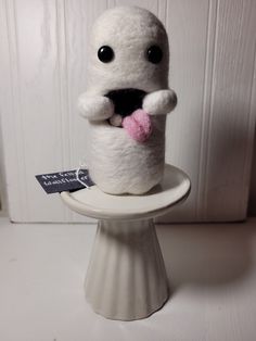 a stuffed animal is sitting on top of a small white pedestal with a tag in it's mouth