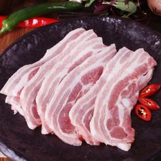 raw meat on a black plate next to peppers and peppercorst in the background