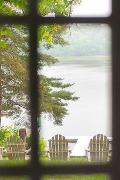 two lawn chairs sitting on top of a lush green field next to a body of water