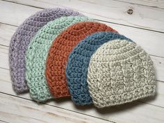 five crocheted hats are lined up on a wooden surface