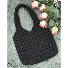 a black crocheted bag sitting on top of a bed next to pink roses