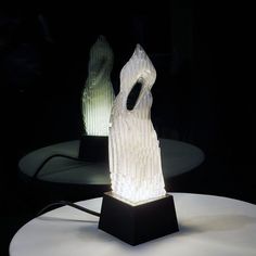 a white sculpture sitting on top of a table next to a black light bulb in the shape of a woman