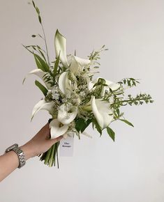 a bouquet of white flowers being held by a woman's hand with bracelets