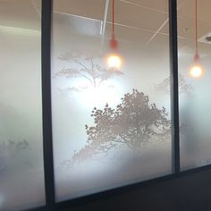 three lamps are hanging from the ceiling in front of frosted glass windows with trees on them