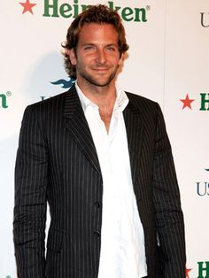 a man standing in front of a white wall wearing a suit and smiling at the camera