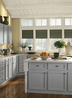 a bowl of oranges sitting on top of a white kitchen counter next to a window