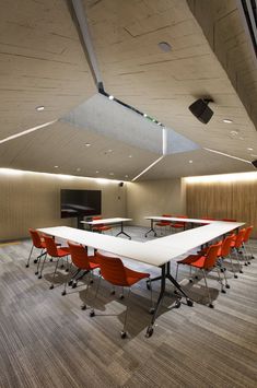 an empty conference room with red chairs and a white table in front of a flat screen tv