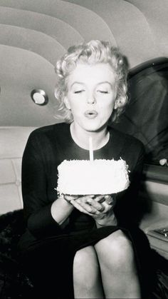 a woman blowing out the candles on her birthday cake while sitting in front of an airplane