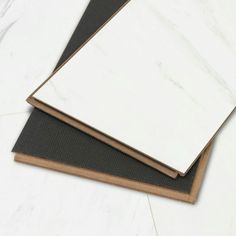 two sheets of white marble sitting on top of each other in front of a black mat