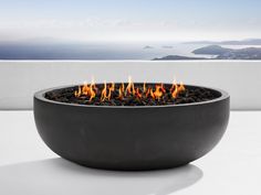 a fire pit sitting on top of a table next to a white wall and ocean