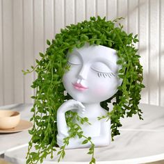 a white statue with green leaves on it's head and eyes, sitting on a table