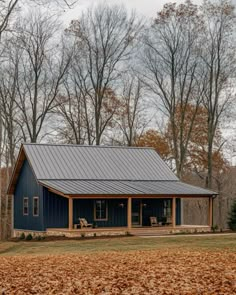 a small blue house with a metal roof in the middle of leaves on the ground