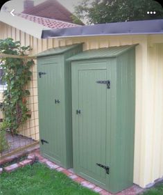 two green storage sheds sitting next to each other on the grass in front of a house