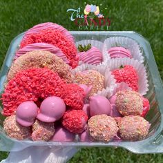 there are many candy candies in the plastic container on the grass, including strawberries and raspberries