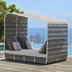 an outdoor daybed with pillows on it next to a pool and the ocean in the background