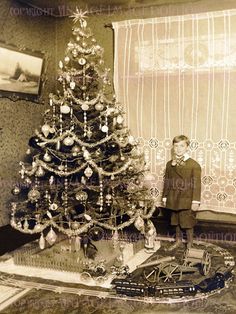 a young boy standing next to a christmas tree in an old fashioned room with a toy train on the floor