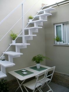 there is a small table and chair under the stairs in this room with plants on it