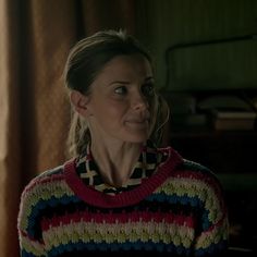 a woman wearing a multicolored sweater stares into the distance