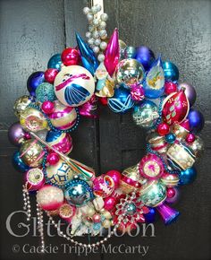 a colorful christmas wreath with ornaments hanging from it's side on a black door