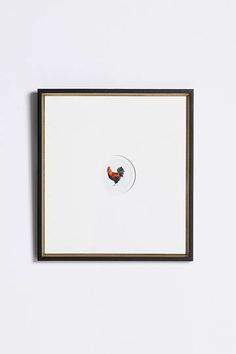 a white wall with a black frame and a red bird in the middle on it