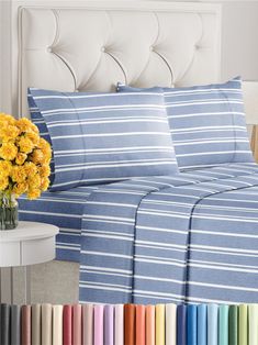 a bed with blue and white striped sheets next to a vase filled with yellow flowers