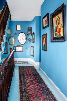 a hallway with blue walls and pictures hanging on the wall, along with a red rug