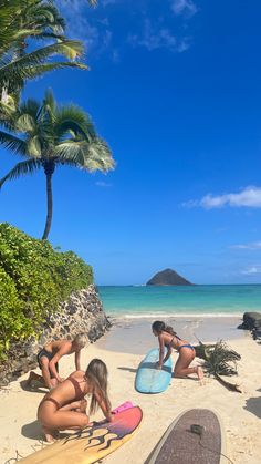 three women sitting on the beach with their surfboards in front of them and palm trees