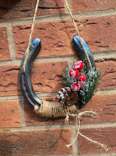 a horseshoe hanging on the side of a brick wall with flowers and pine cones in it