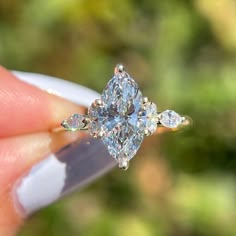 a woman's hand holding an engagement ring with three pear shaped diamonds