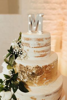 a white and gold wedding cake with the letter m on top