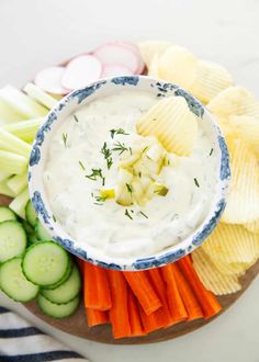 a bowl of dip surrounded by vegetables and crackers on a platter with chips