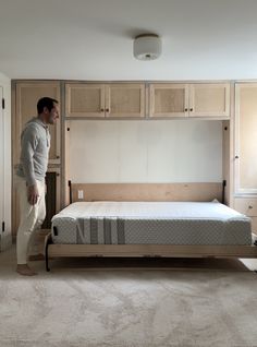 a man standing next to a bed in a room with beige carpet and wooden cabinets