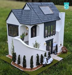 a doll house with a car parked in front of it on the grass near a fence