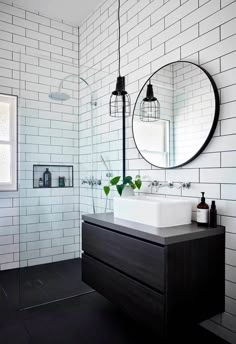 a bathroom with white brick walls and dark wood vanity, round mirror above the sink