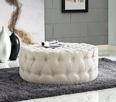 a white ottoman sitting on top of a gray rug in a living room next to a vase