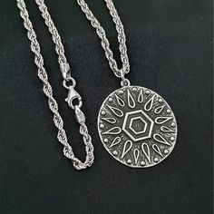 a silver necklace with an intricate design on the front and back, sitting on a black surface