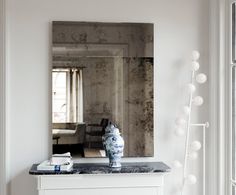 a white dresser topped with a blue and white vase sitting next to a large mirror