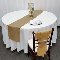 a round table with two chairs and a white table cloth draped over the top, along with a vase filled with flowers